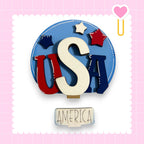 a circular arrangement of the letters 'USA' in red, white, and blue, with a heart-shaped object and stars on the edges. Below the arrangement, the word "AMERICA" is written.