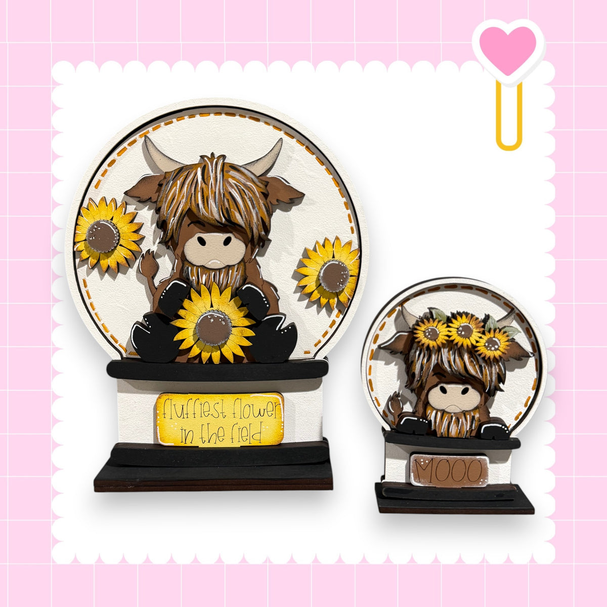 a decorative snow globe with a cow and sunflowers on it. The snow globe is placed on a stand, and there is a heart-shaped sticker on the right side of the image.