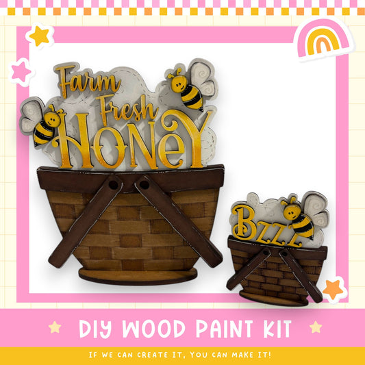a DIY wood paint kit for creating a farm fresh honey basket. The kit includes a wooden basket and a bee figurine, along with the text "Farm Fresh Honey" and "BZZZ" indicating the contents of the basket. The kit is presented in a pink and yellow frame, and the text "DIY WOOD PAINT KIT" is displayed at the bottom.