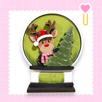 A snow globe containing a reindeer wearing a Santa hat and scarf, with a Christmas tree inside, and the text "DEER CROSSING AHEAD" on the base.