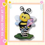 A wooden paint kit depicting a smiling bee holding a kite, with a pink and yellow border.