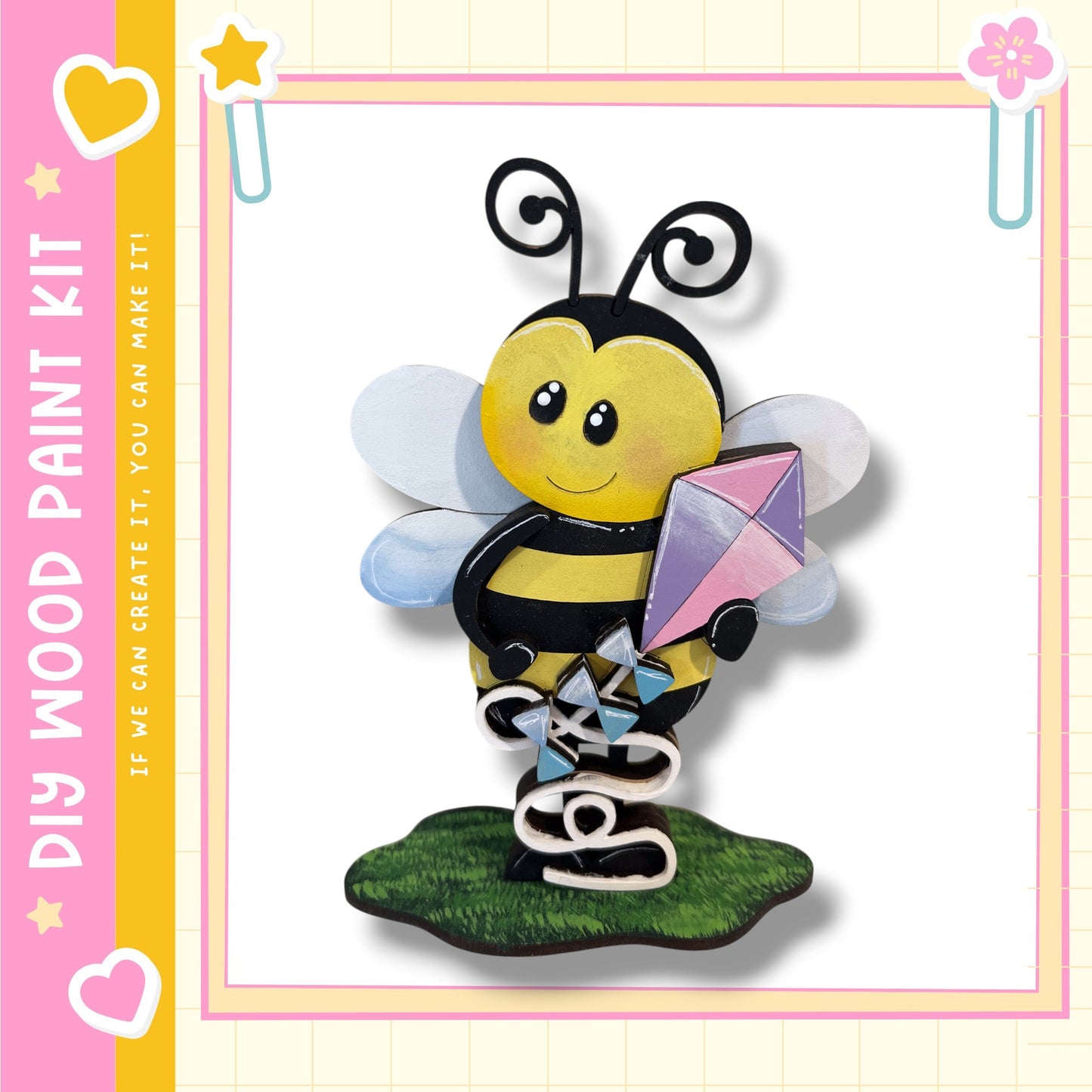 A wooden paint kit depicting a smiling bee holding a kite, with a pink and yellow border.