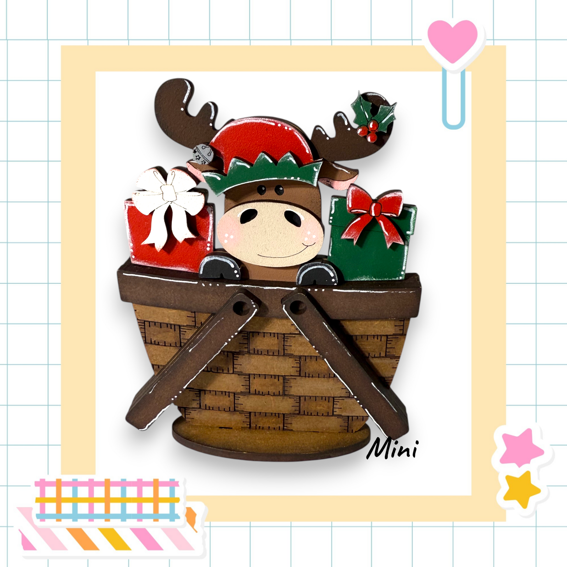A wooden moose figurine wearing a Santa hat and holding a basket of presents, set against a grid background with a pink heart and a star sticker.