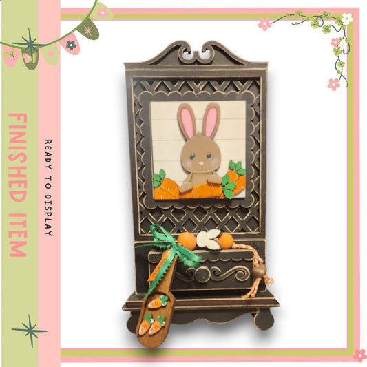 A wooden frame with a picture of a rabbit inside, surrounded by carrots and other decorative elements.