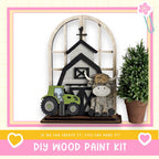 a DIY wood paint kit, including a wooden barn, tractor, and a stuffed animal cow. The barn is made of wood and has a black roof, while the tractor is painted green. The cow is also painted green and has a brown mane. The image is framed by a pink border, and there is a heart and a flower in the corners. The text at the bottom of the image reads "If we can create it, you can make it!"
