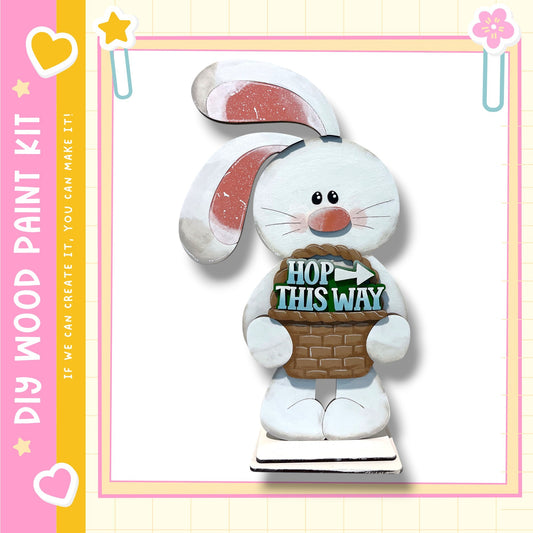 A wooden Easter bunny figurine holding a basket with the text "HOP THIS WAY" written on it.