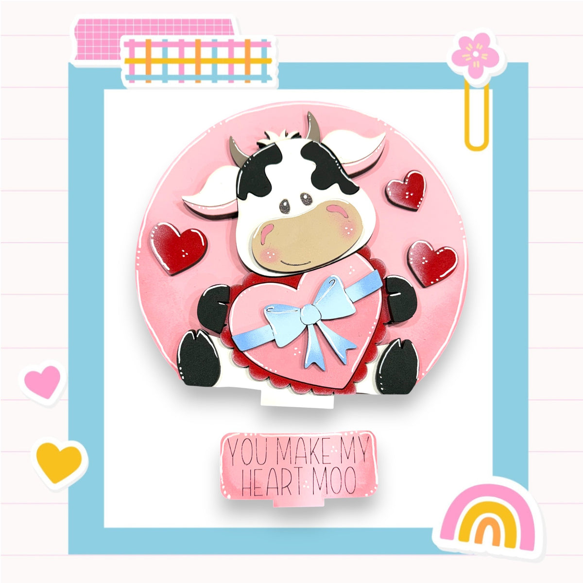 A heart-shaped cake with a cow figure on it, surrounded by red hearts, and a sign that says "You make my heart moo".