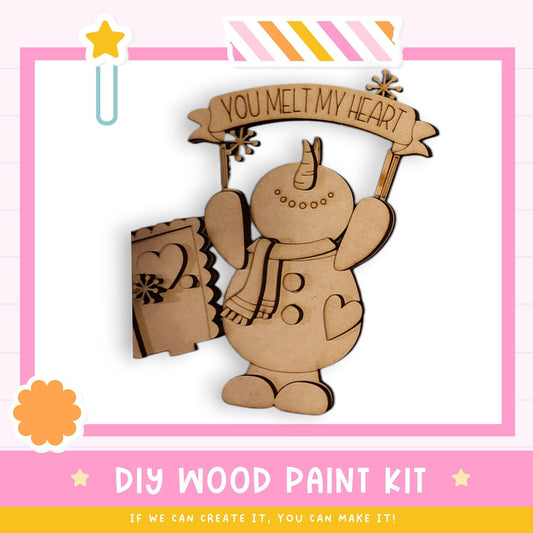 a DIY wood paint kit for creating a wooden snowman. The kit includes a wooden snowman figure and a banner that says "You melt my heart".