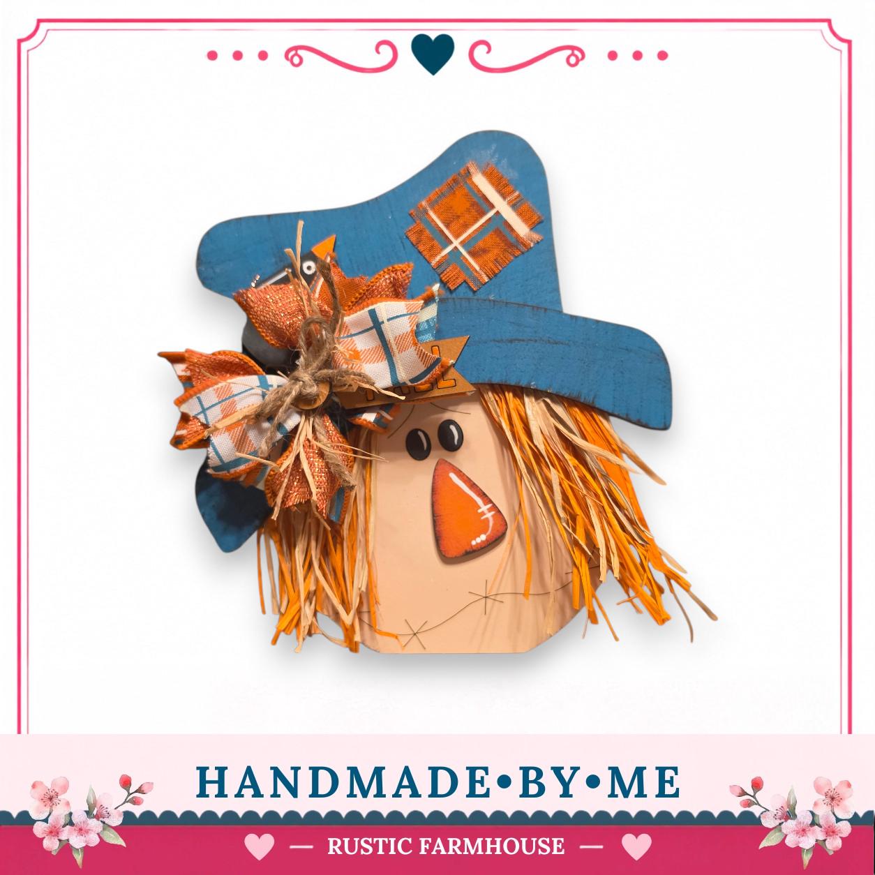 A handmade scarecrow with a blue hat, orange and white plaid cloth, and a red nose, set against a white background.