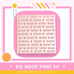 The image is a promotional poster for a DIY wood paint kit. It features a pink background with a repeating pattern of the word "XOXO" in various sizes and colors. The text "DIY WOOD PAINT KIT" is prominently displayed, along with the phrase "IF WE CAN CREATE IT, YOU CAN MAKE IT!" at the bottom of the image.