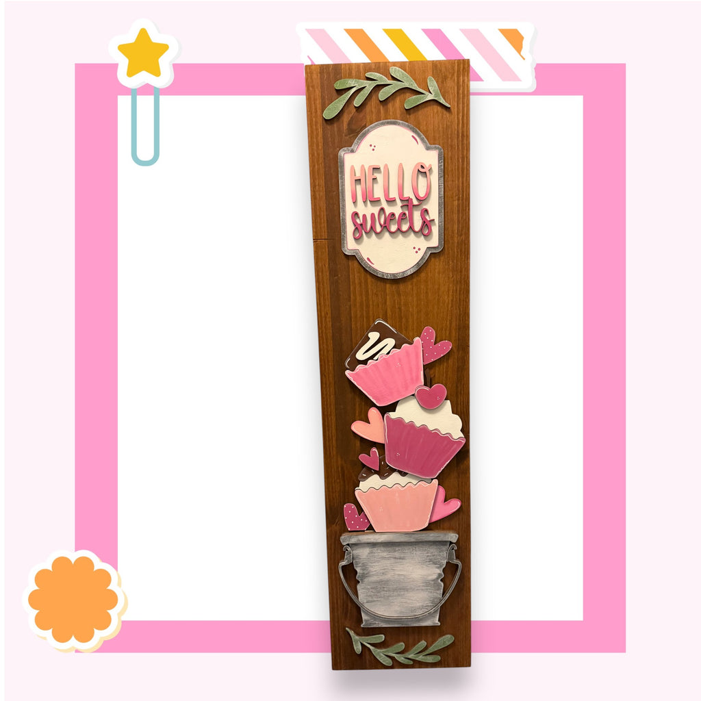 a wooden frame with a decorative design, including a sign that says "Hello sweets" and various cupcake-like shapes.