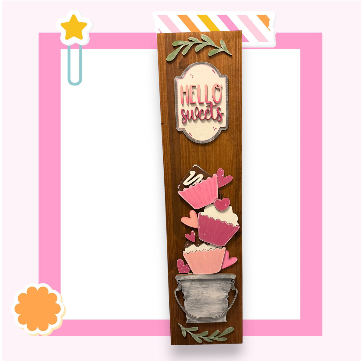 a wooden frame with a decorative design, including a sign that says "Hello sweets" and various cupcake-like shapes.