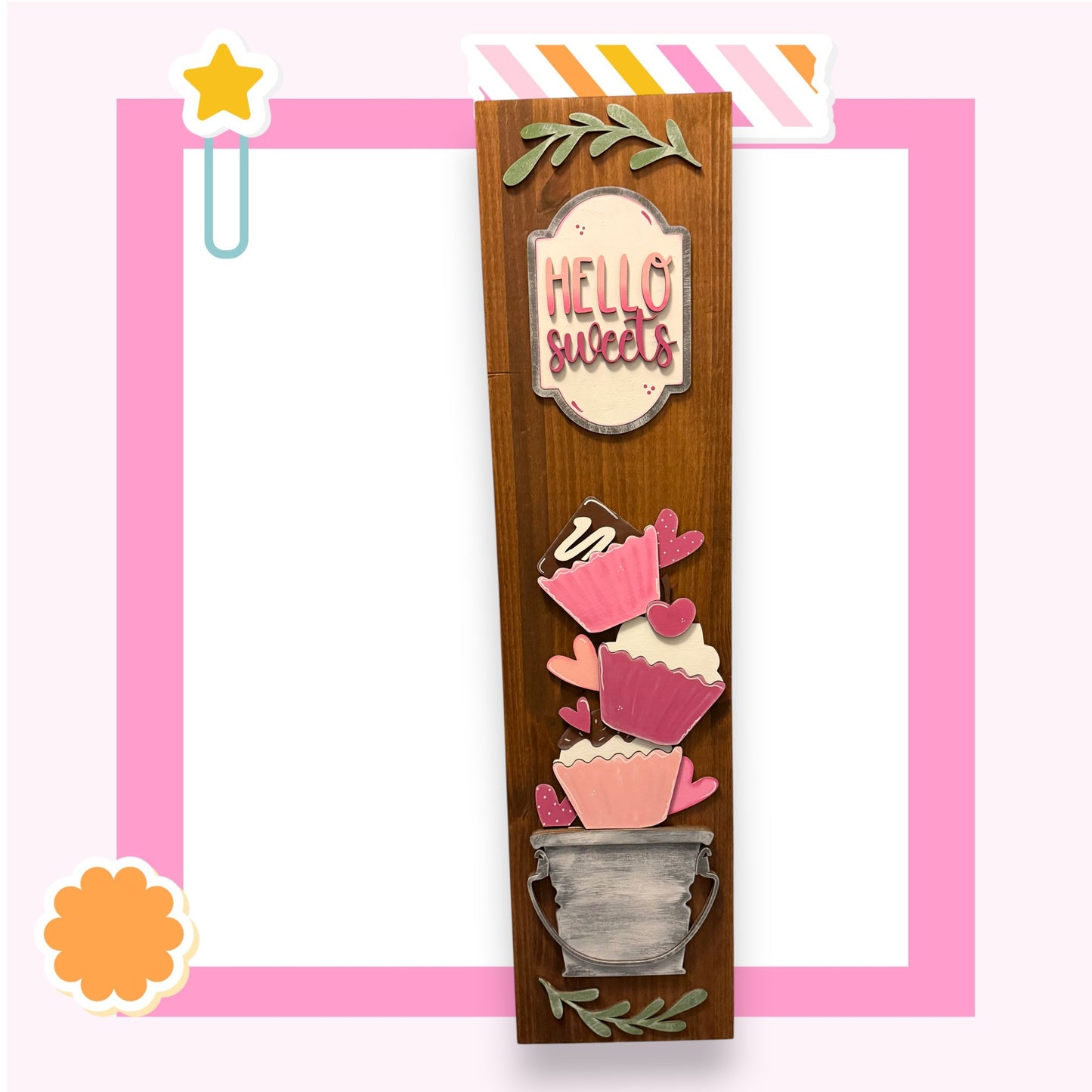 a wooden frame with a decorative design, including a sign that says "Hello sweets" and various cupcake-like shapes.