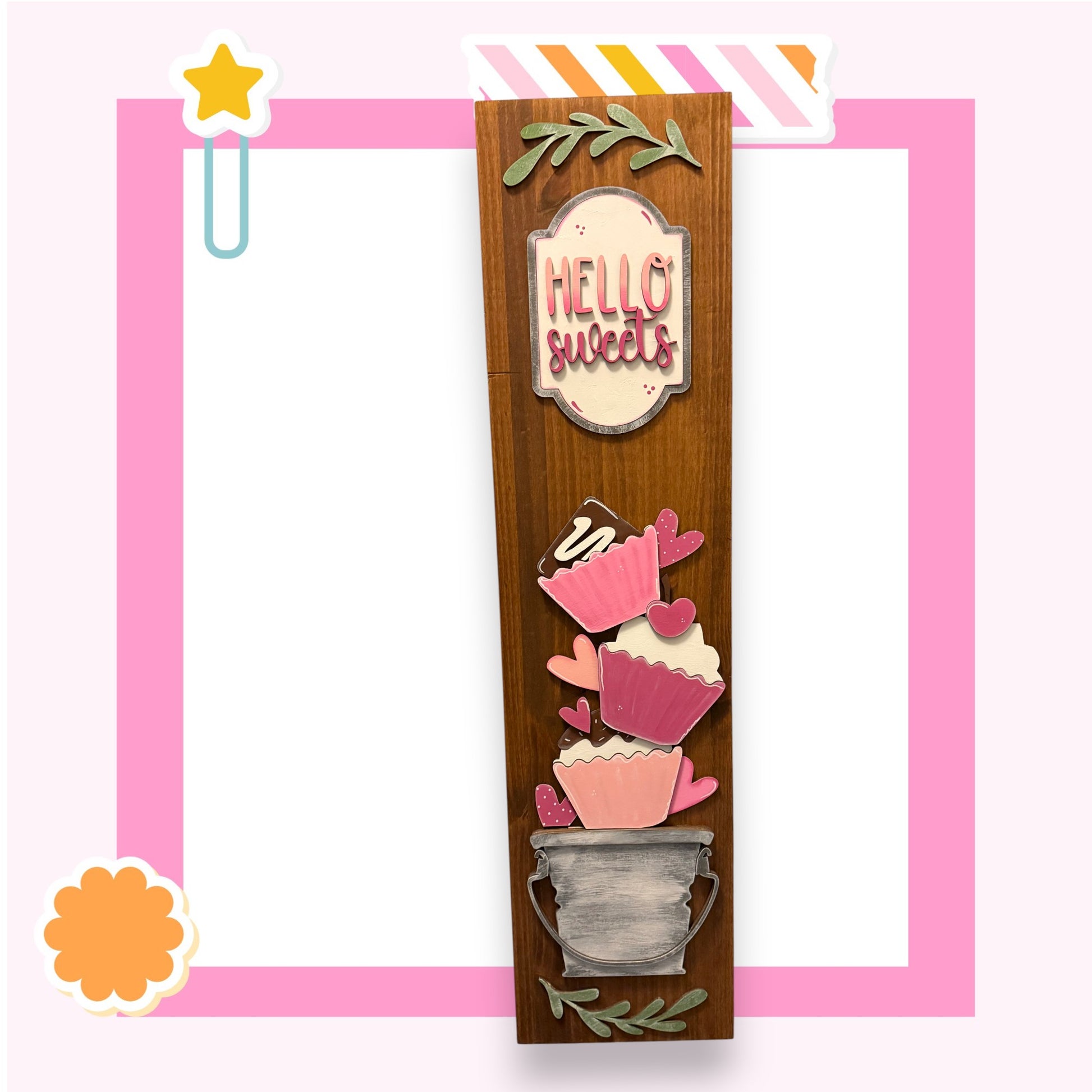 a wooden frame with a decorative design, including a sign that says "Hello sweets" and various cupcake-like shapes.