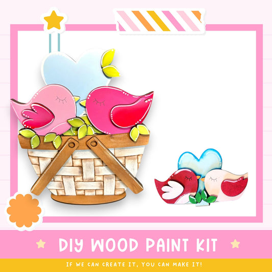 The image is a colorful and whimsical DIY wood paint kit featuring a basket filled with painted wooden birds, a heart-shaped bird, and a flower. The kit appears to be designed for creating custom wooden bird ornaments, with the promise that if the viewer can create it, they can make it.
