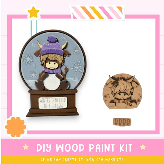 a DIY wood paint kit for creating a snow globe, with a wooden snow globe containing a cartoon cow wearing a purple hat and a sign that says "Winter is better on the farm".