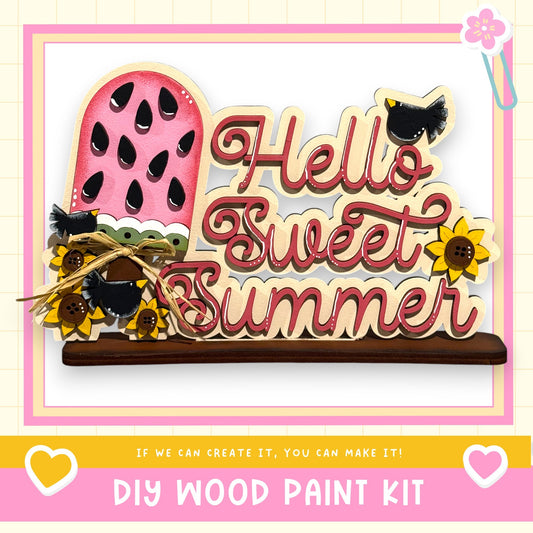 The image is a colorful and decorative DIY wood paint kit featuring a wooden sign with the text "Hello Sweet Summer" and various decorative elements such as sunflowers and a watermelon.