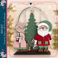A DIY kit featuring a Christmas tree and two wooden figures, one of Santa Claus and the other of an elderly woman, likely representing the characters from the Christmas story.