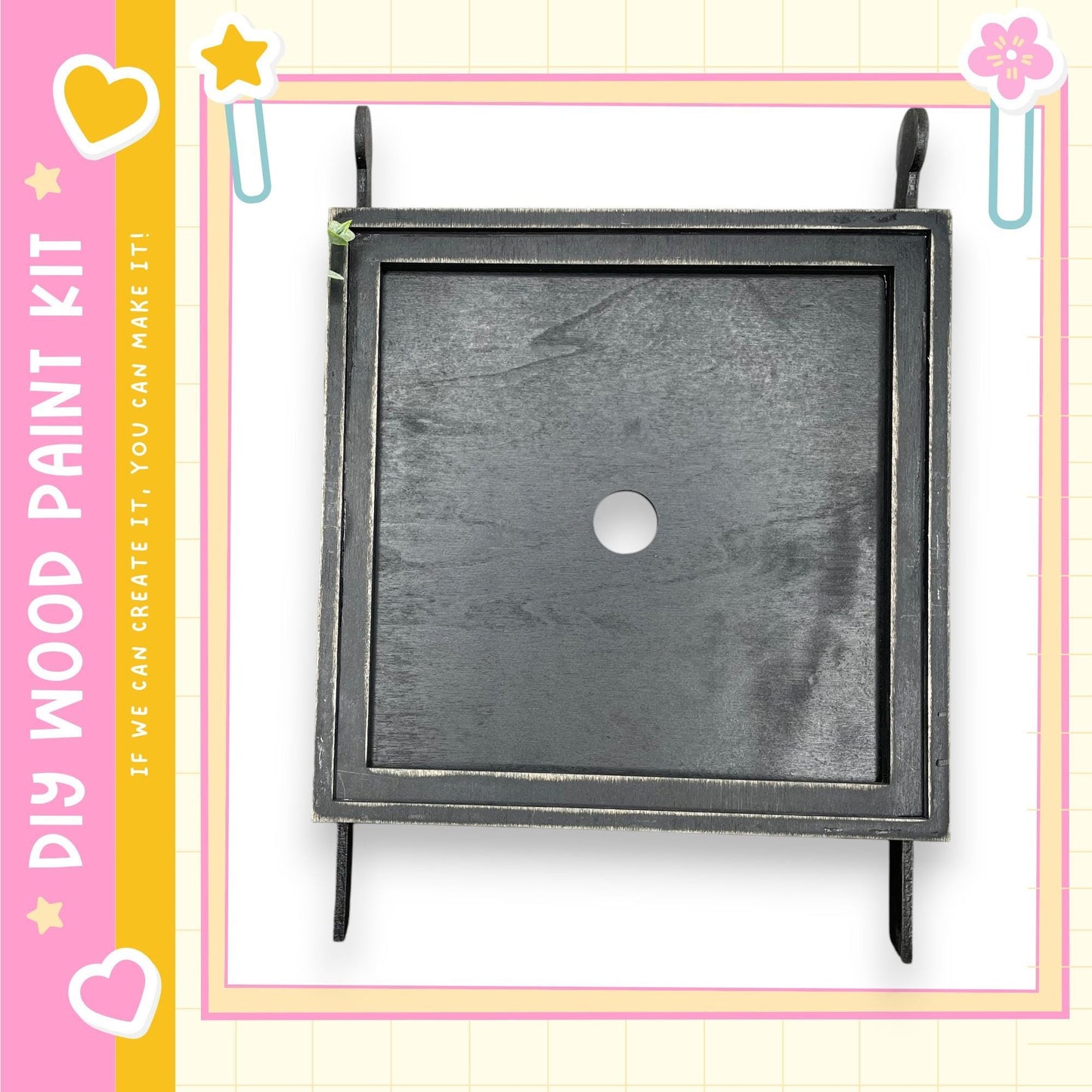 a black square frame with a white circular hole in the center, set against a pink and yellow background with decorative elements.
