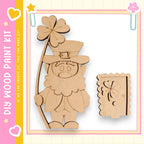 A wooden cutout of a leprechaun holding a four-leaf clover, with a door cutout next to it, all set against a pink and yellow background.