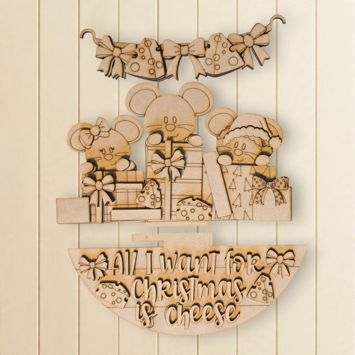 A wooden decoration with a Christmas theme, featuring three cartoon mice and a bow. The decoration also includes a text that says "All I want for Christmas is cheese".