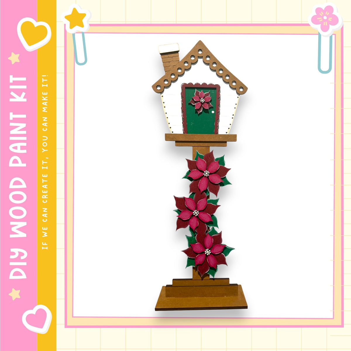 A wooden house-shaped decoration with a green door and pink flowers hanging from the roof.