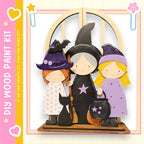 A wooden paint kit depicting three cartoon-style girls dressed as witches, with a black bat and a black cat as props.