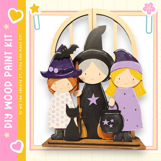 A wooden paint kit depicting three cartoon-style girls dressed as witches, with a black bat and a black cat as props.