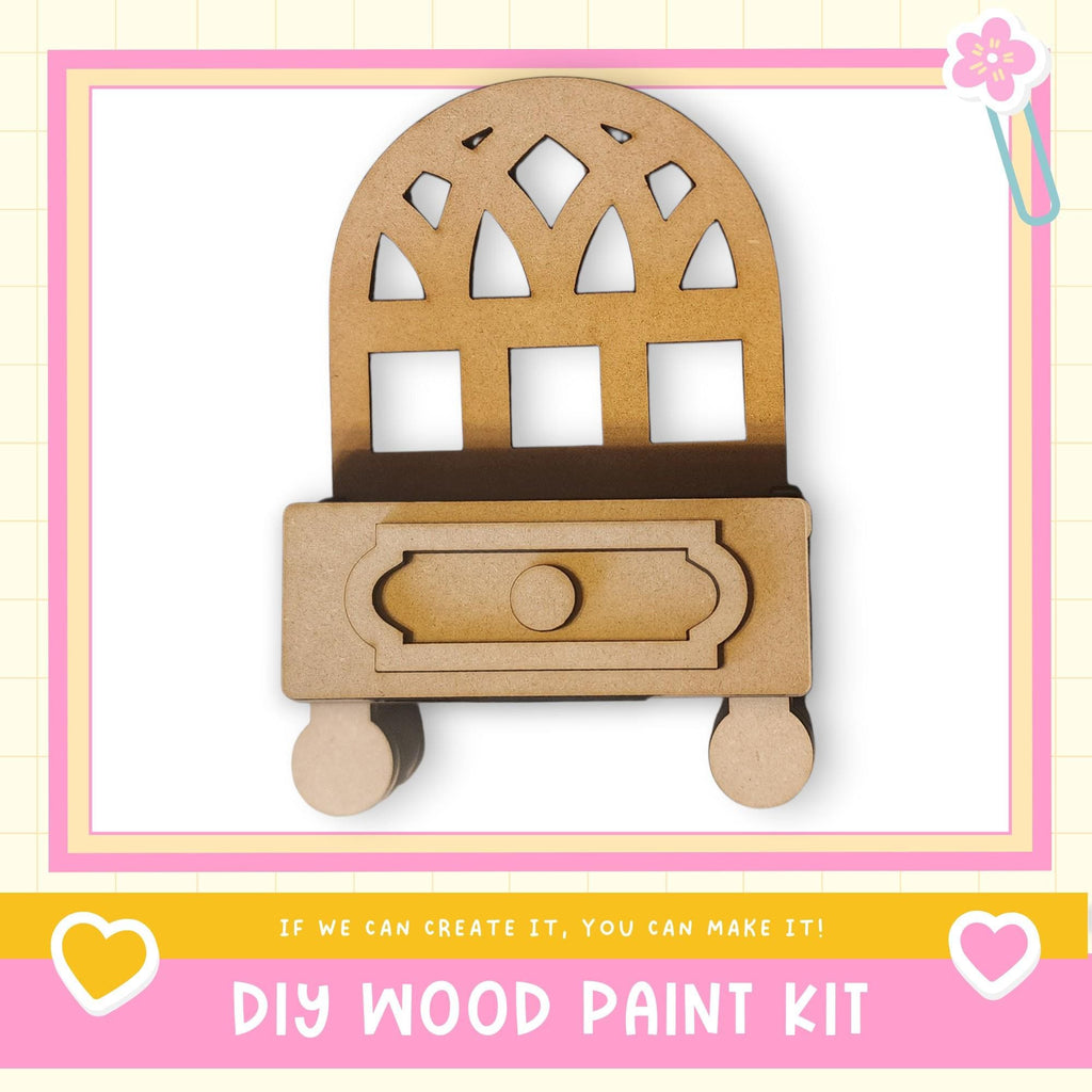 a DIY wood paint kit, with a wooden cabinet or shelf depicted in the center. The kit appears to be made of wood and has a drawer. The image is framed with a pink border and includes a heart symbol on the left side. The text "DIY WOOD PAINT KIT" is displayed at the bottom of the image.