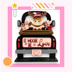 A wooden truck with a moose figure and various heart-shaped objects, including a pink heart and a red heart, on the back. The truck has a sign that says "It Moose Be Love".