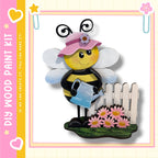 A wooden paint kit depicting a smiling bee holding a watering can, standing next to a white picket fence with pink flowers.
