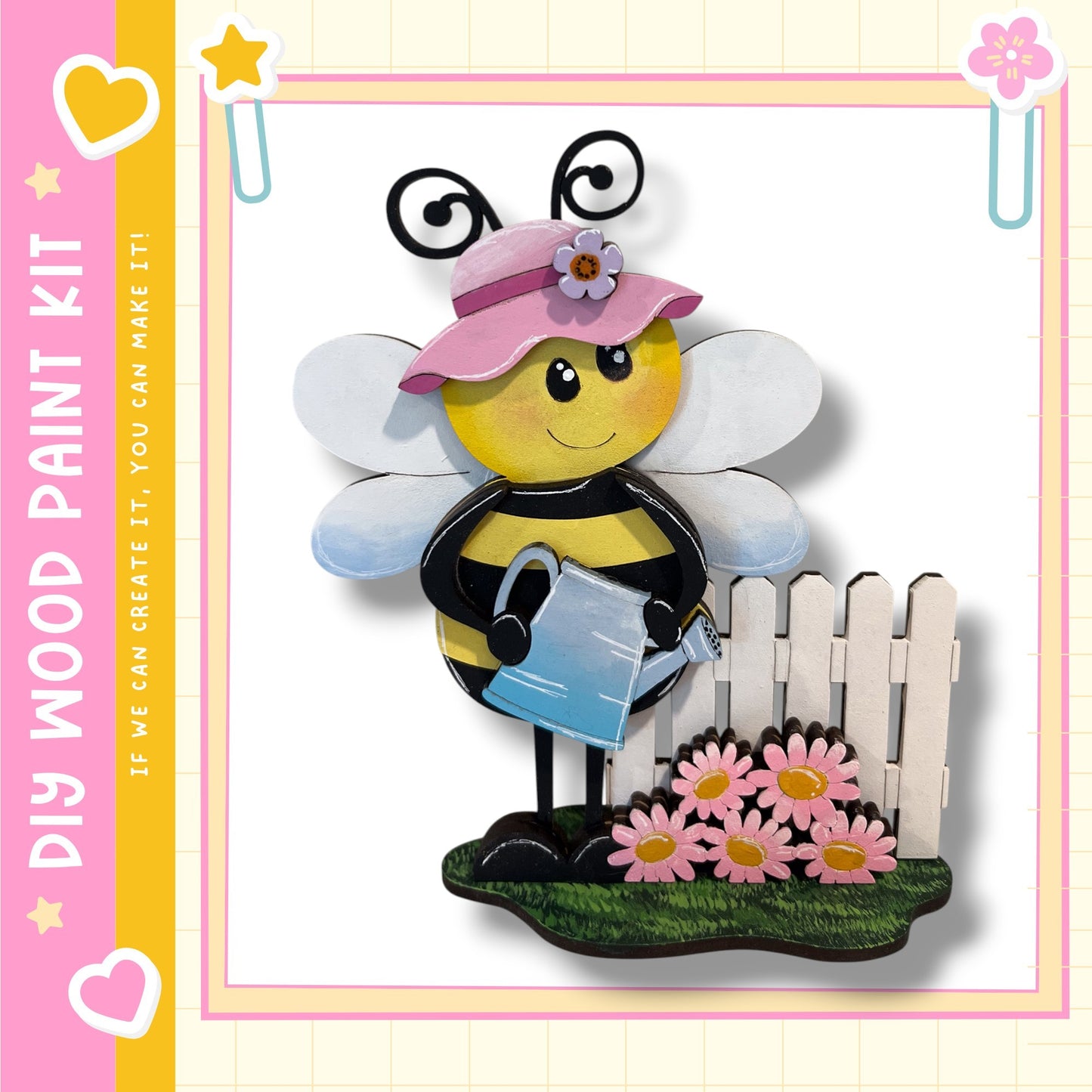 A wooden paint kit depicting a smiling bee holding a watering can, standing next to a white picket fence with pink flowers.