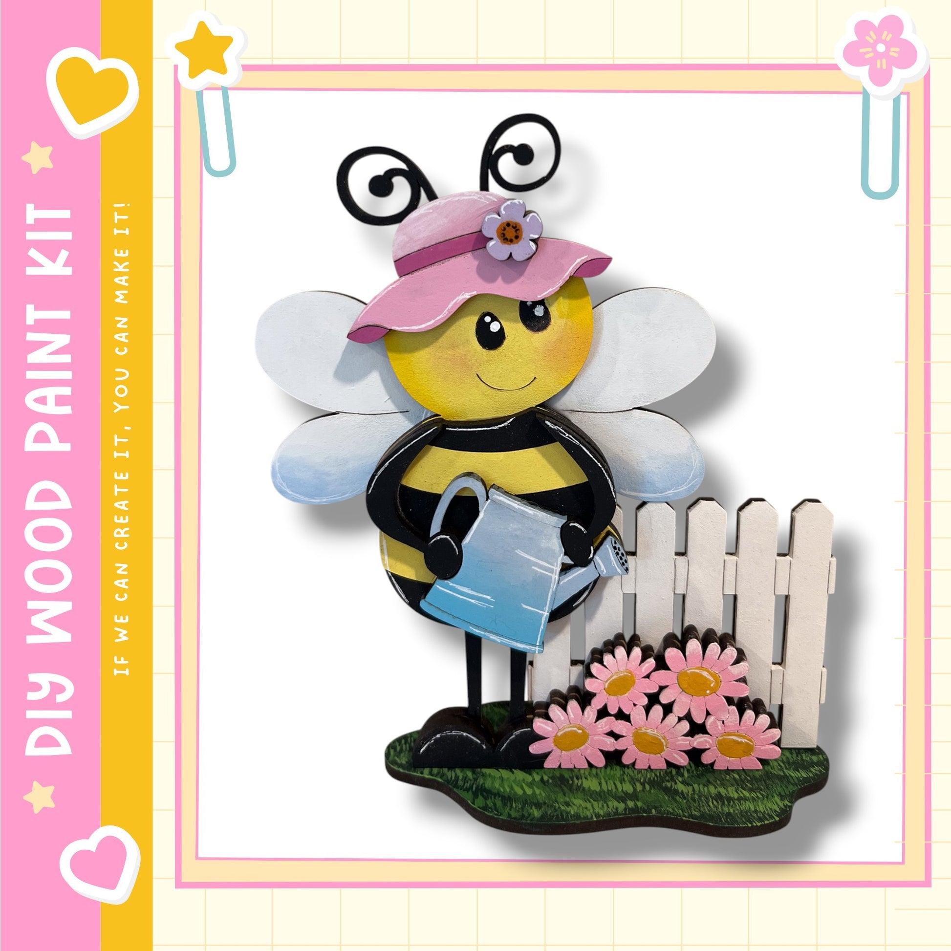 A wooden paint kit depicting a smiling bee holding a watering can, standing next to a white picket fence with pink flowers.