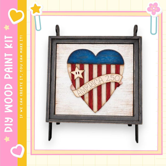 a heart-shaped cutout of the American flag, with the words "AMERICA 250" written on it. The heart is made of wood and is displayed in a black frame.