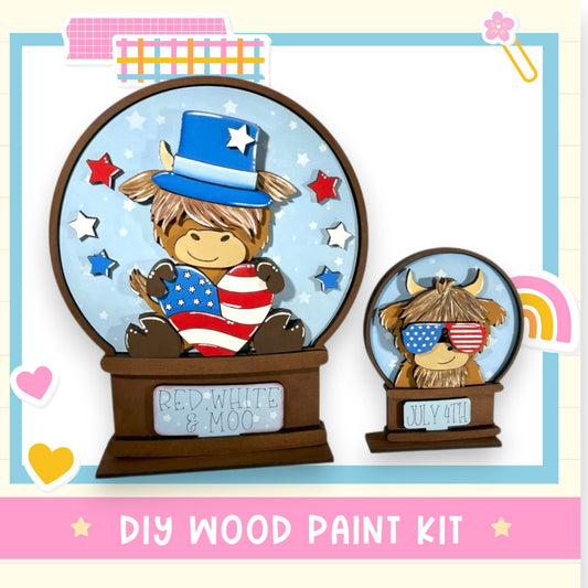 a DIY wood paint kit for creating a wooden snow globe with a patriotic theme. The snow globe depicts a cow wearing a patriotic hat and glasses, surrounded by stars and a rainbow. The kit includes a label that reads "DIY WOOD PAINT KIT" and "RED WHITE & MOON".