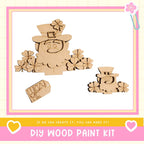 a DIY wood paint kit with a focus on creating a wooden cutout of a leprechaun. The kit includes a wooden cutout of a leprechaun, a tag with the word "Lucky Me", and a heart-shaped tag. The kit is presented in a pink and yellow frame, and the text encourages viewers to "If we can create it, you can make it!"