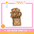 a DIY wood paint kit with a heart-shaped cutout and the word "XOXO" written on it, set against a pink and white background.