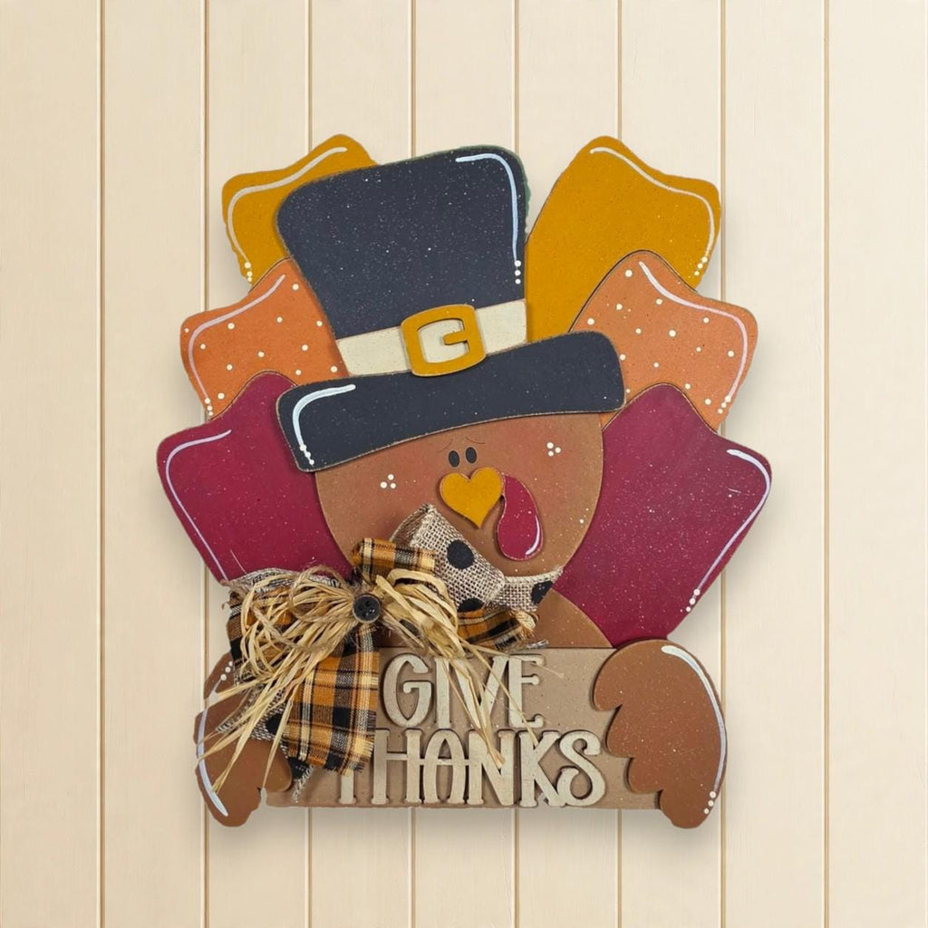 A wooden sign with a turkey wearing a top hat and holding a sign that says "Give Thanks".