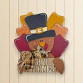A wooden sign with a turkey wearing a top hat and holding a sign that says "Give Thanks".