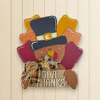A wooden sign with a turkey wearing a top hat and holding a sign that says "Give Thanks".