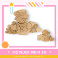 a DIY wood paint kit for creating wooden snowmen, with a pink and white striped border and a star decoration.