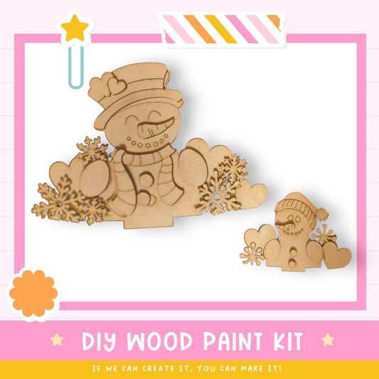 a DIY wood paint kit for creating wooden snowmen, with a pink and white striped border and a star decoration.