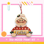 A wooden ornament in the shape of a woman holding a cookie sheet, with the word "Cookies" written on it. The ornament is hanging from a string and is part of a DIY wood paint kit.