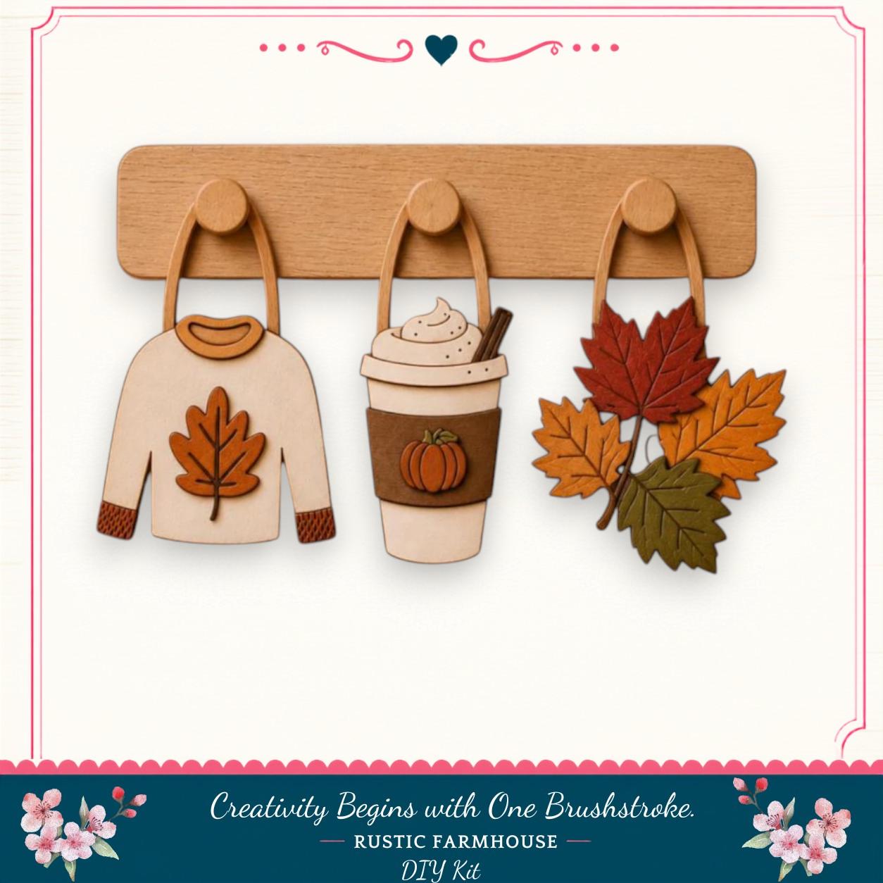 a wooden hanger with three decorative items hanging on it: a sweater with a leaf design, a coffee cup with a pumpkin and whipped cream design, and a leaf arrangement.