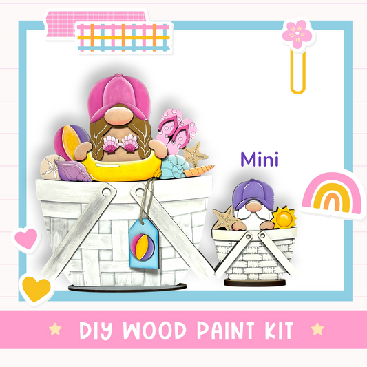 The image is a colorful illustration of two wooden gnome figurines, one larger and one smaller, sitting in baskets filled with various objects such as seashells, starfish, and a beach ball. The image also includes a text box that reads "DIY WOOD PAINT KIT" and a small rainbow graphic.