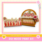 a DIY wood paint kit for creating a wooden sign or decoration with the words "barn fresh berries" written on it. The kit includes a wooden frame and a wooden sign with the text "barn fresh berries" written on it. The kit is presented in a pink and yellow color scheme, with a heart symbol and a flower symbol in the corners.