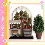 a wooden apple orchard with a tree filled with red apples, a wooden cart selling apples, and a potted plant. The scene is set against a pink and yellow background with a heart and star motif.