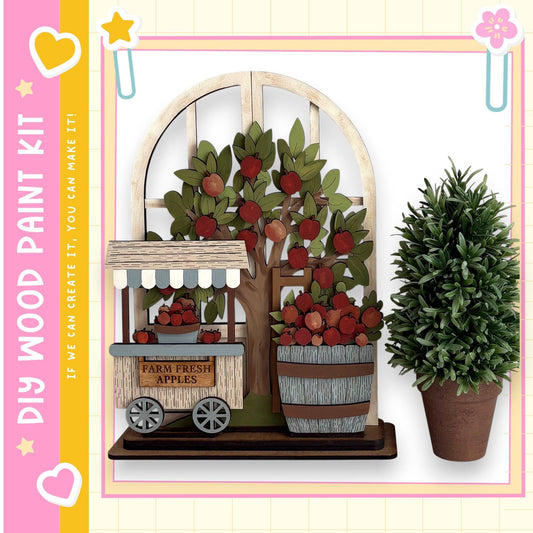 a wooden apple orchard with a tree filled with red apples, a wooden cart selling apples, and a potted plant. The scene is set against a pink and yellow background with a heart and star motif.