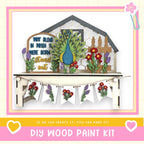 The image is a colorful and whimsical DIY wood paint kit featuring a wooden house, a peacock, and various flowers and plants. The kit appears to be made of wood and is displayed on a shelf. The text "DIY WOOD PAINT KIT" is prominently featured, along with a motivational message encouraging creativity and the ability to make one's own projects.