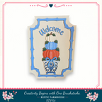 a welcome sign with a decorative design, including a vase with pumpkins and leaves, and the text "Welcome" written on it.